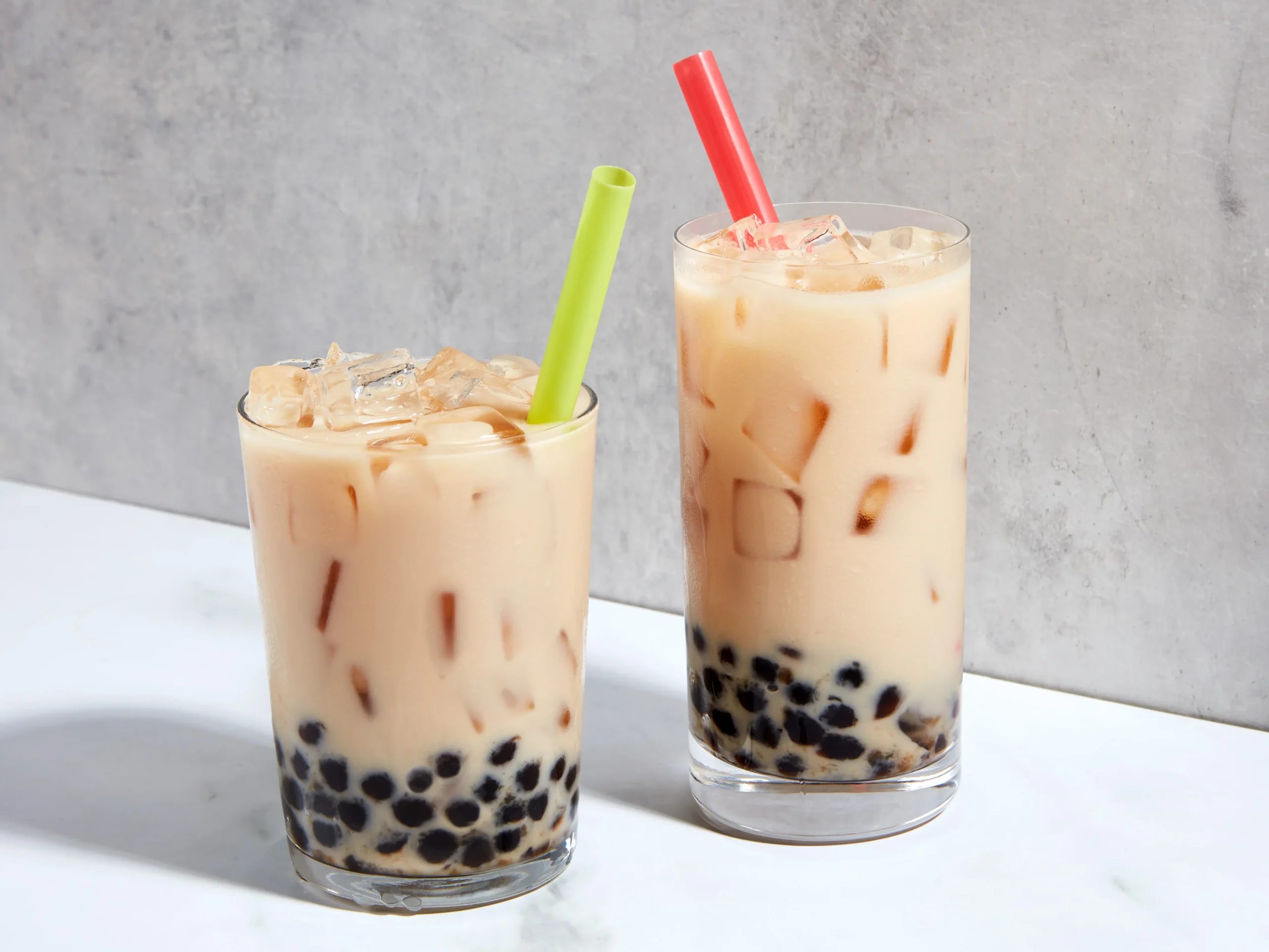 Two glasses are filled with tan colored tea and dark tapioca balls at the bottom.